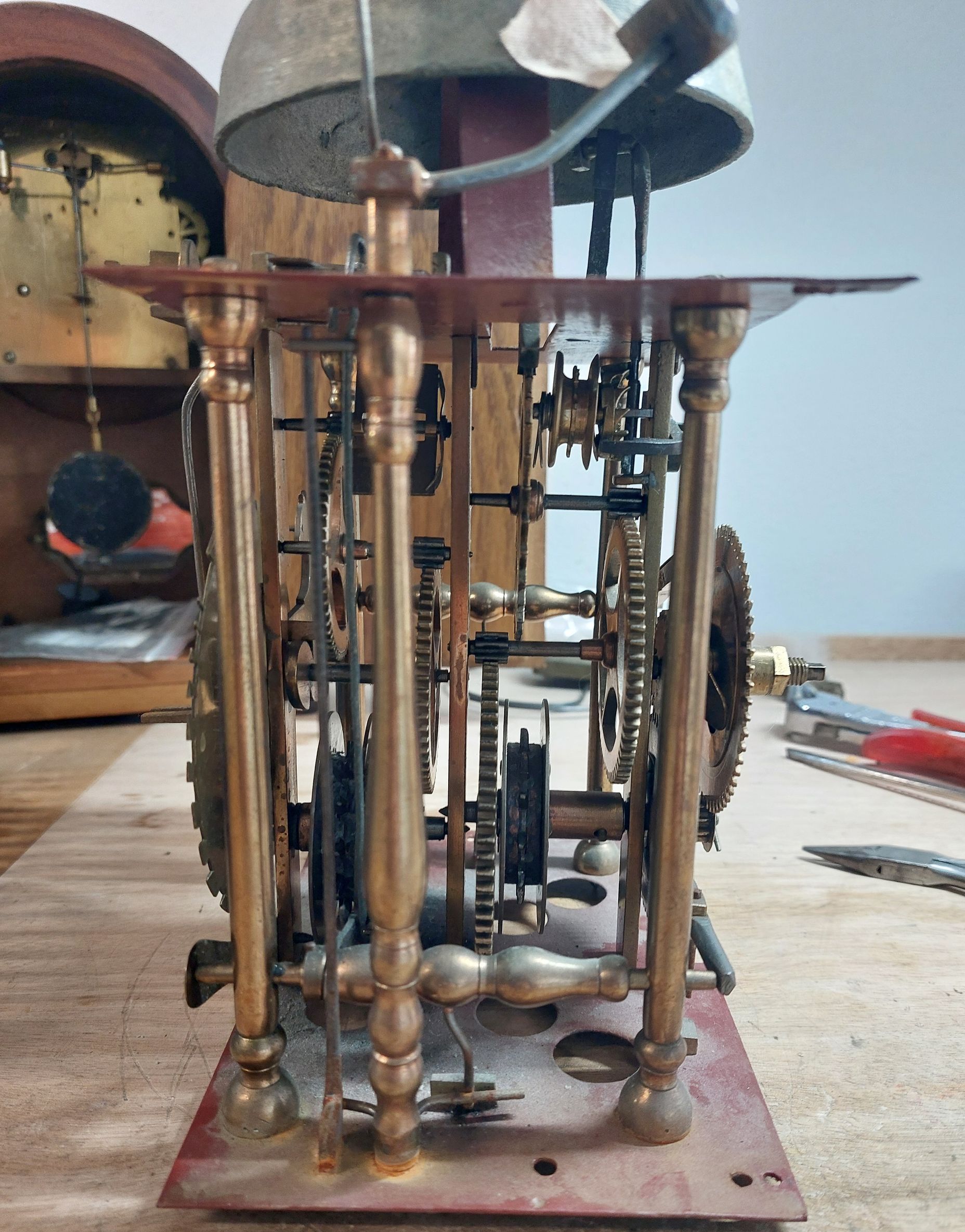 Uurwerkmechanisme met messing onderdelen, tandwielen en bel. Geplaatst op een werkbank.