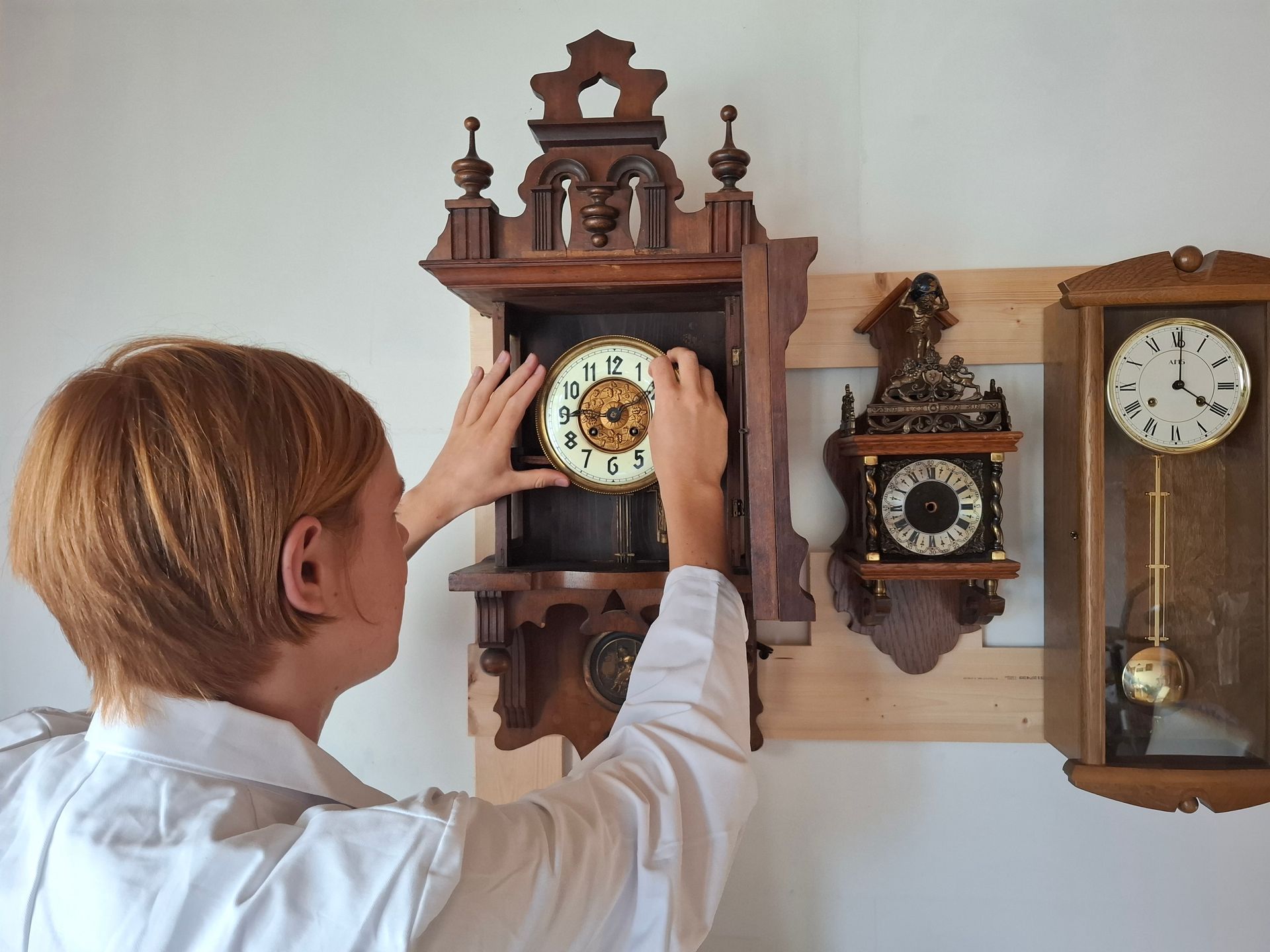 de wijzerplaat van een antieke houten klok aan de muur te verstellen, samen met twee andere klokken.
