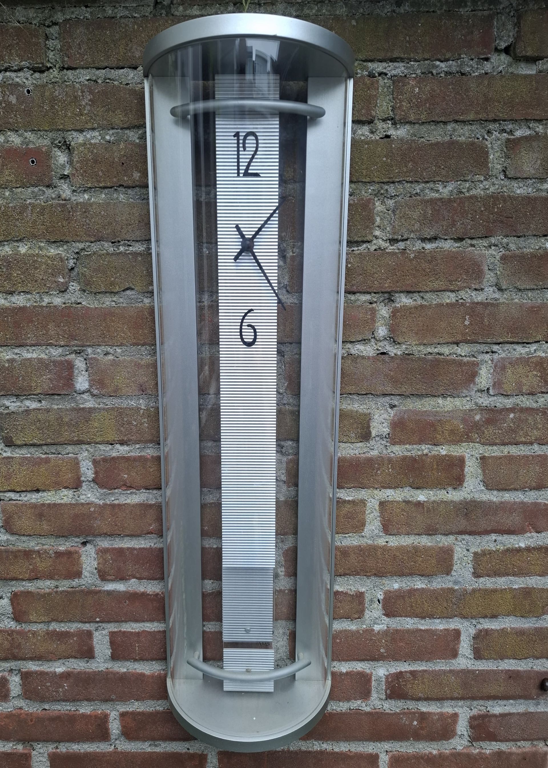 Zilveren en heldere wandklok op een rode bakstenen muur.