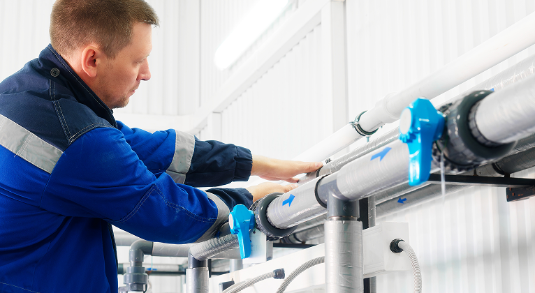 Um homem está trabalhando em um cano em uma fábrica.