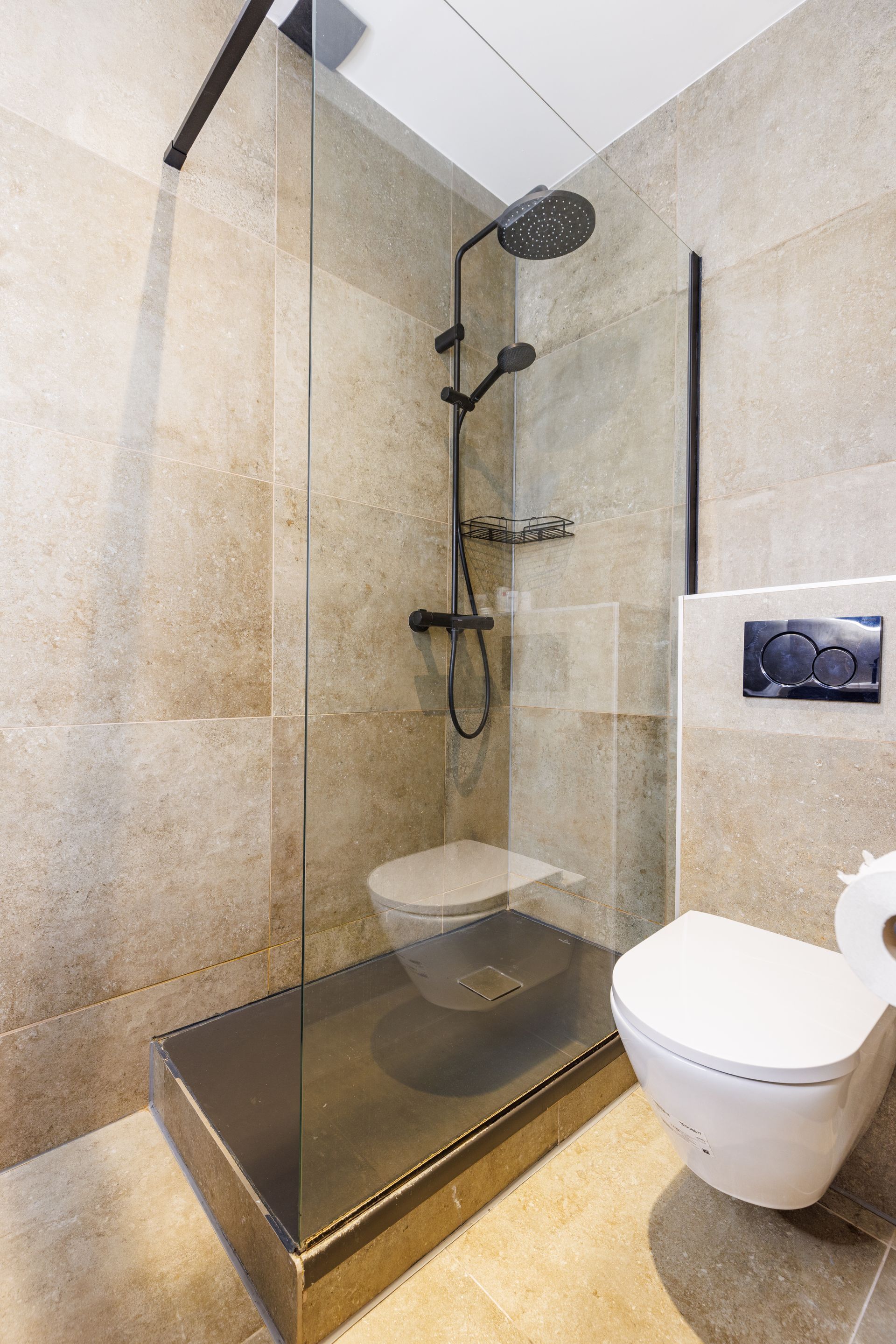 A modern bathroom featuring a walk-in shower with a black fixture and glass partition next to a wall-mounted white toilet.