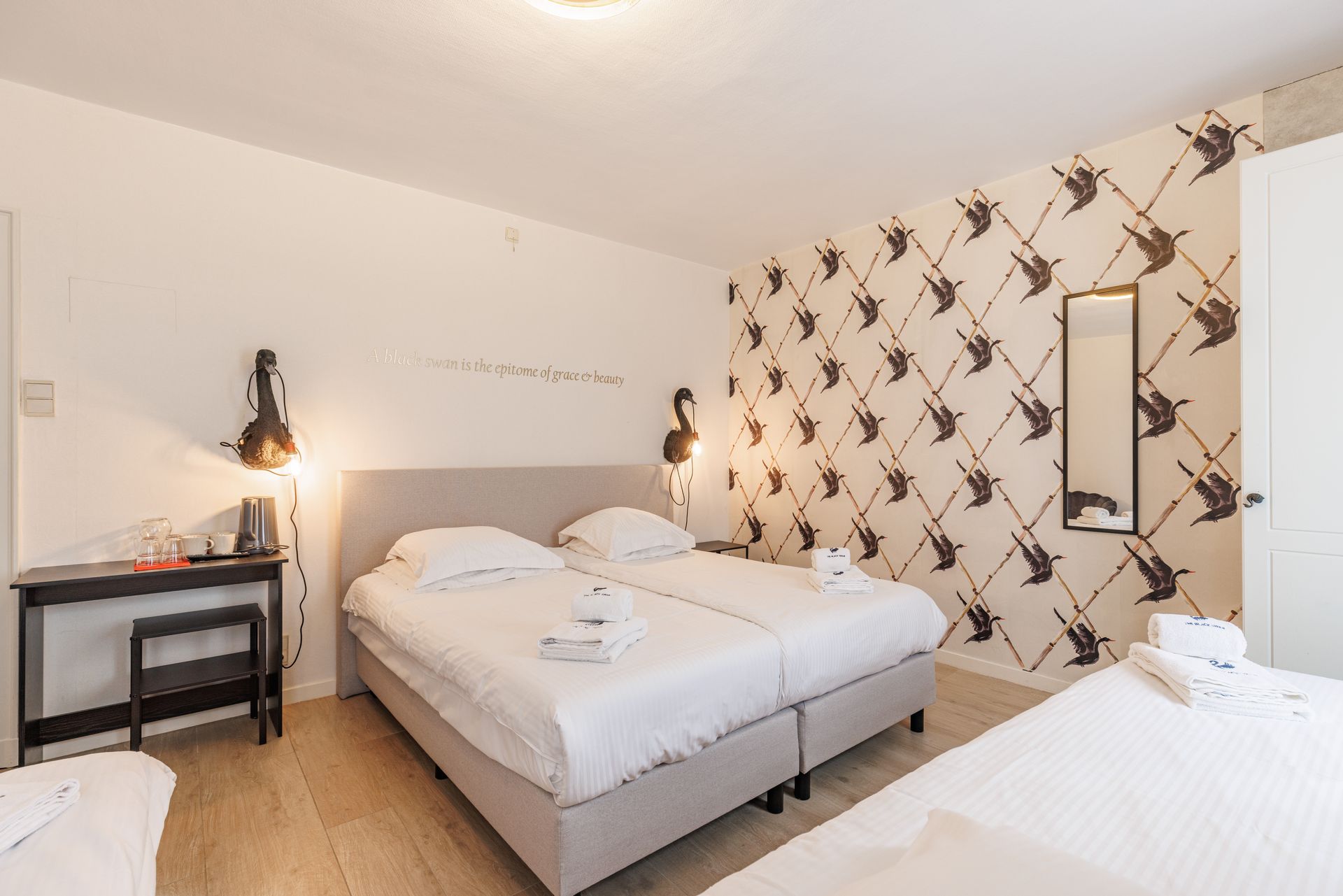 A hotel room with two single beds pushed together, a desk with a stool, and a wall with a bird-patterned wallpaper.