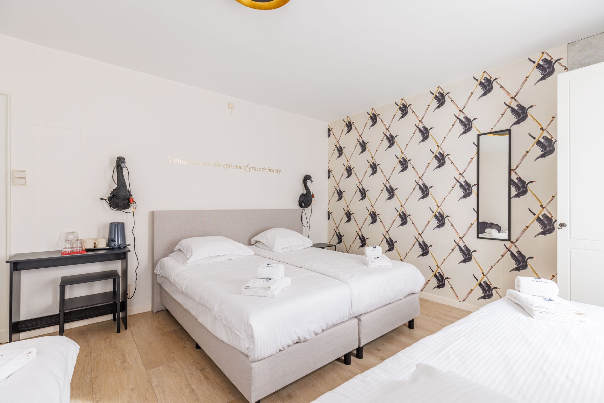 A bedroom with two twin beds joined together, a desk with a kettle, and a wall featuring a patterned bird-print wallpaper.