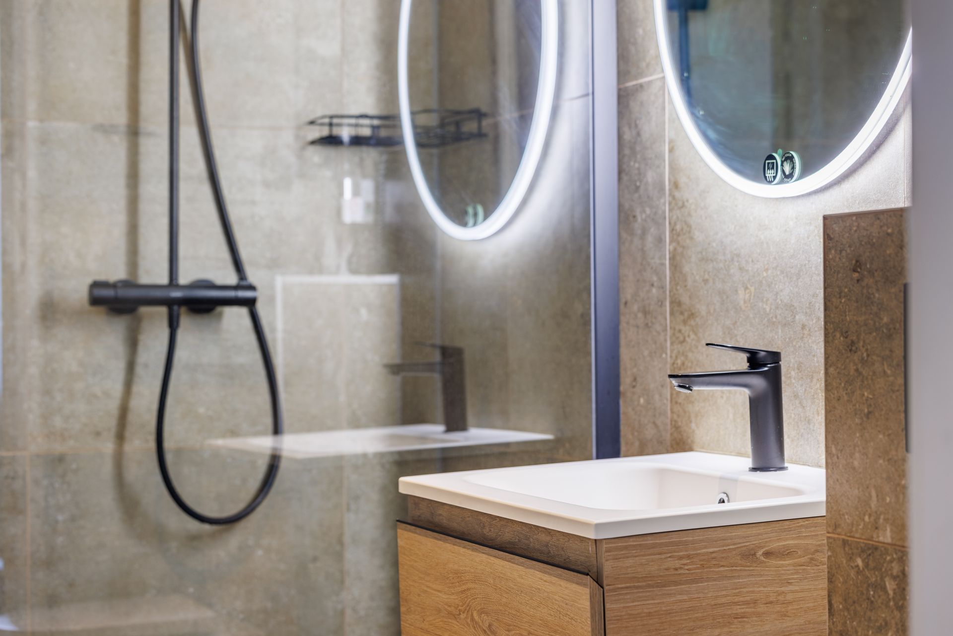 A modern bathroom featuring a white vanity with a black faucet, a backlit circular mirror, and a glass-enclosed shower.