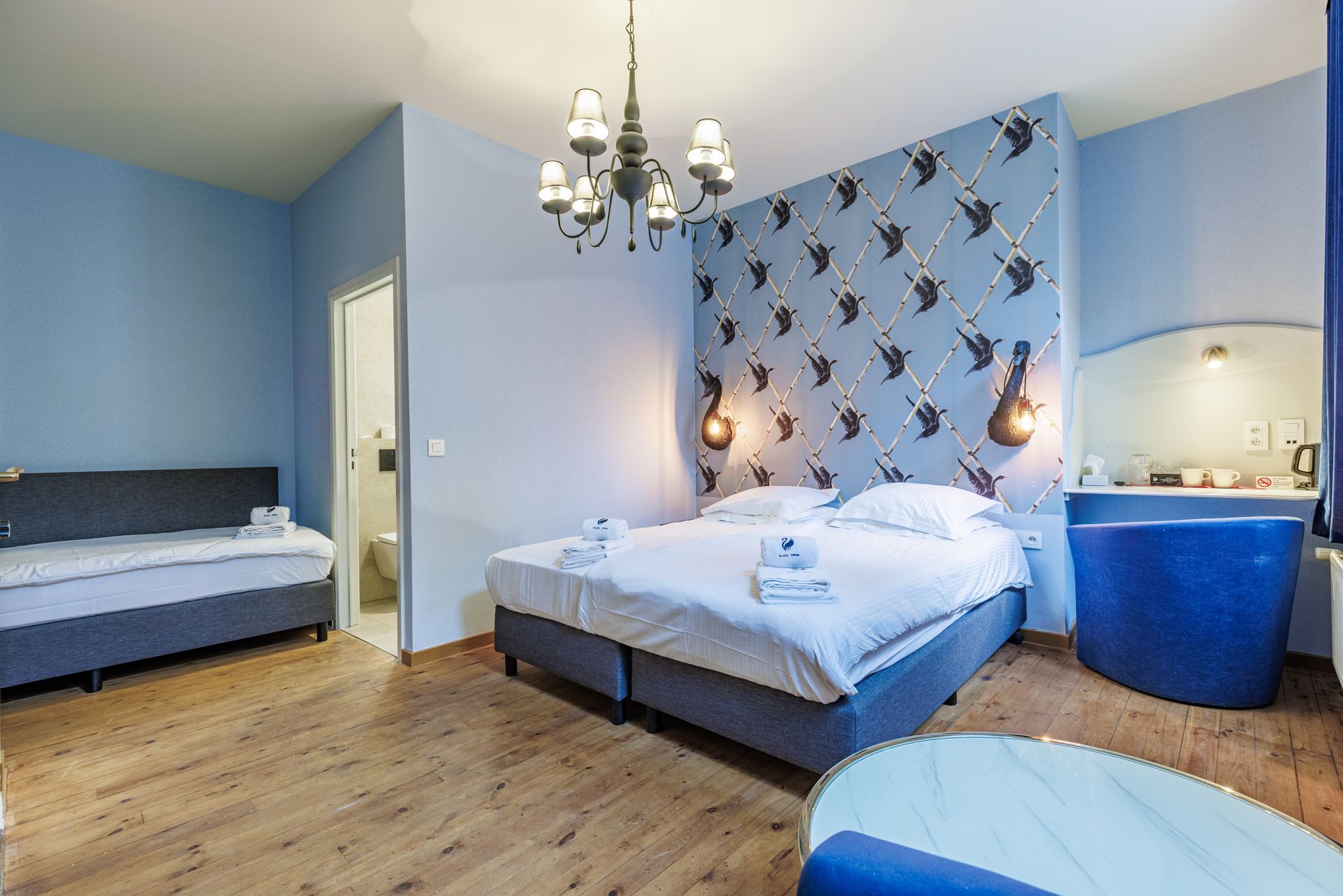 A hotel room with a double bed, a sofa bed, a blue soaking tub, and walls decorated with bird-patterned wallpaper.