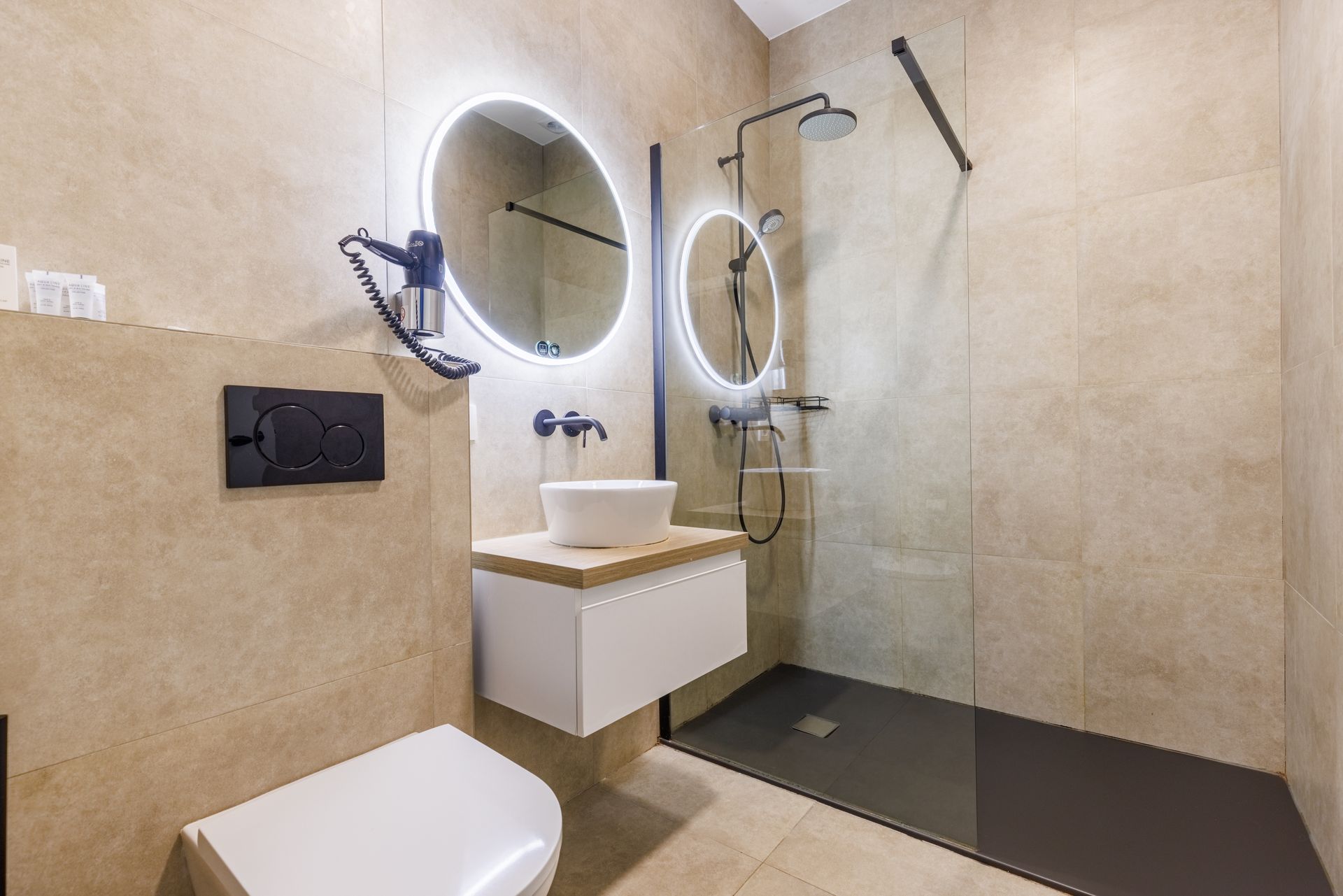 Modern bathroom with a white vessel sink, vanity, wall-mounted toilet, and a glass-enclosed shower with beige tile walls.
