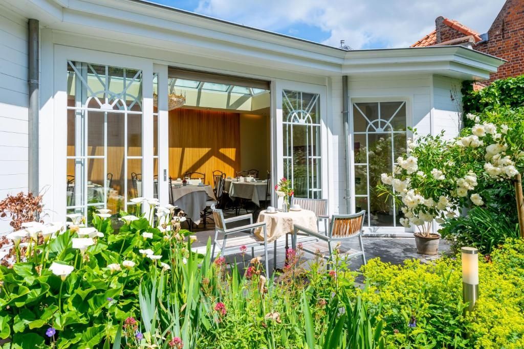 A garden terrace featuring outdoor seating, white rose bushes, and a small statue against a white wall.