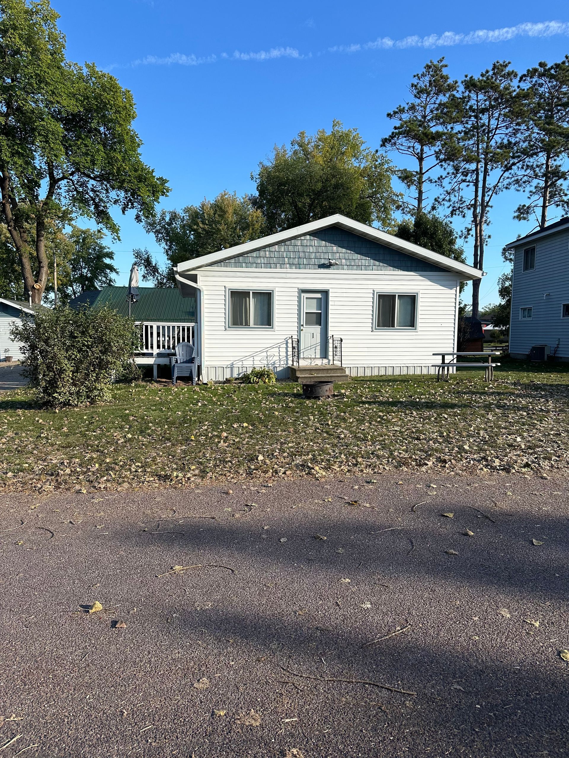 White cottage with two windows, a door, and a porch, set in front of trees and a blue sky.
