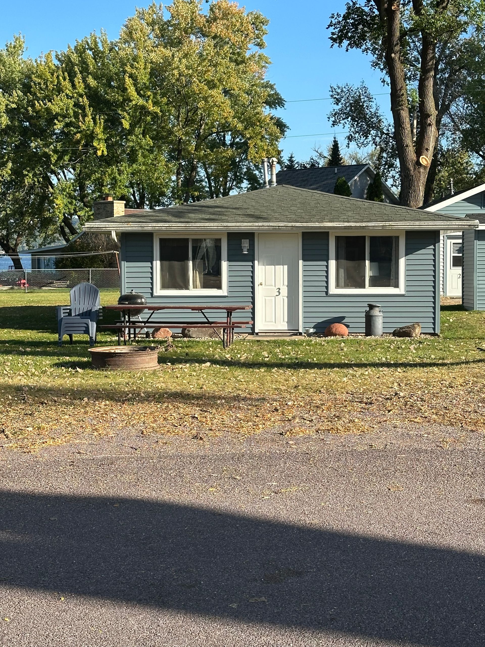 Blue lakeside cabin with white trim, door, and windows. Grassy yard, gravel drive.