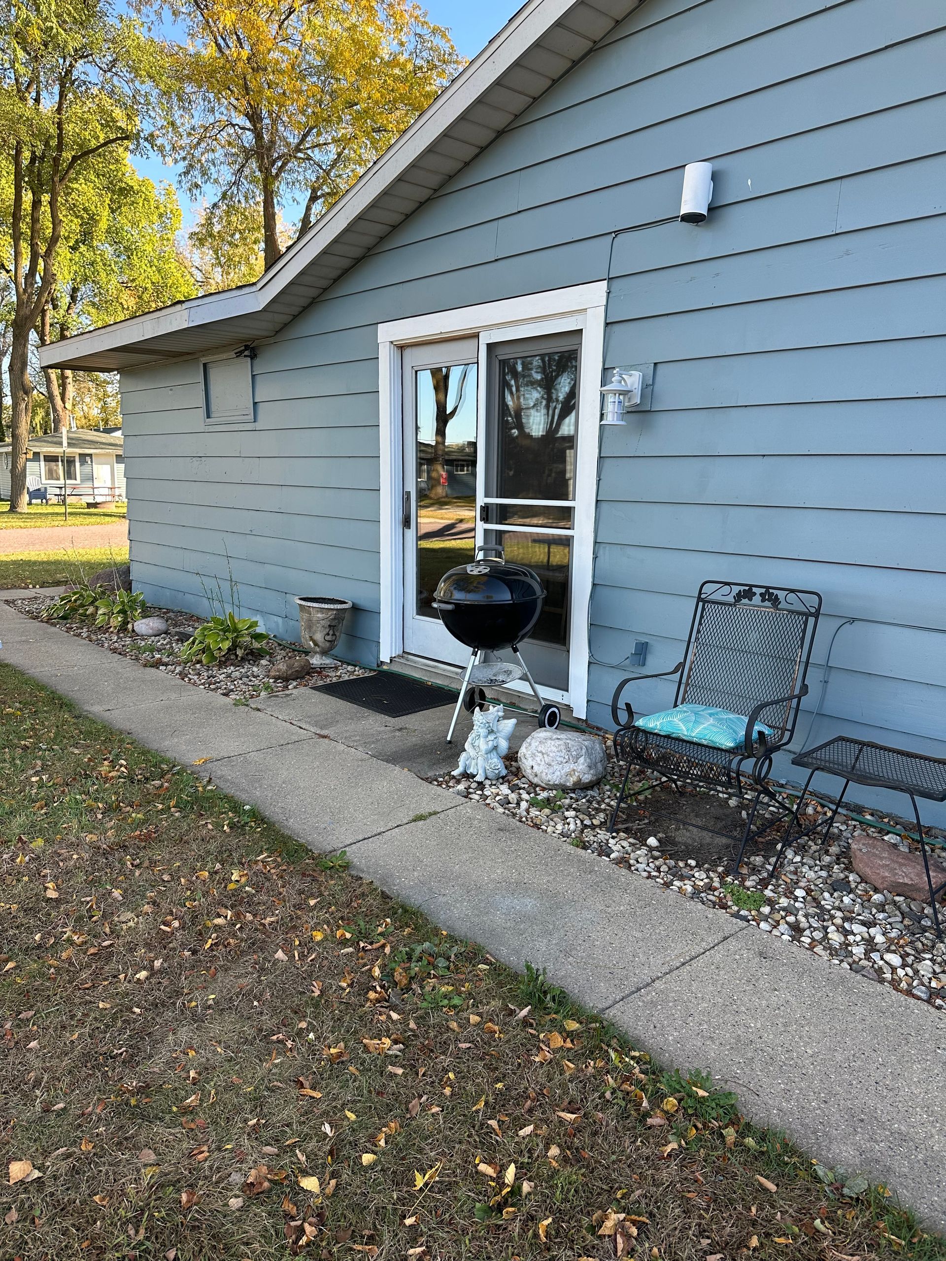 Side of a blue house with a sliding glass door, a grill, and an outdoor chair on a concrete path.