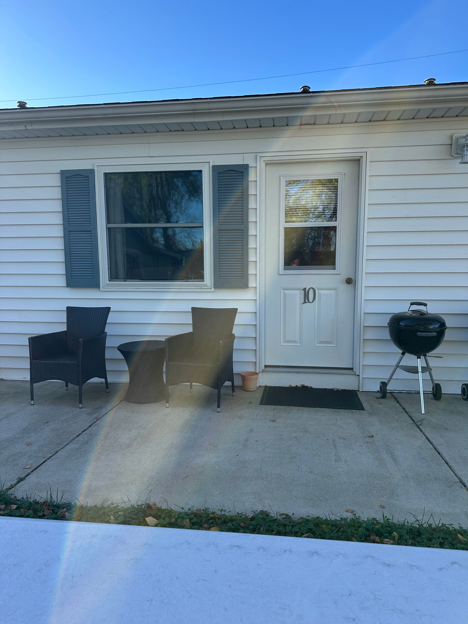 White building exterior with window and door, two chairs, grill, and snow on the ground.