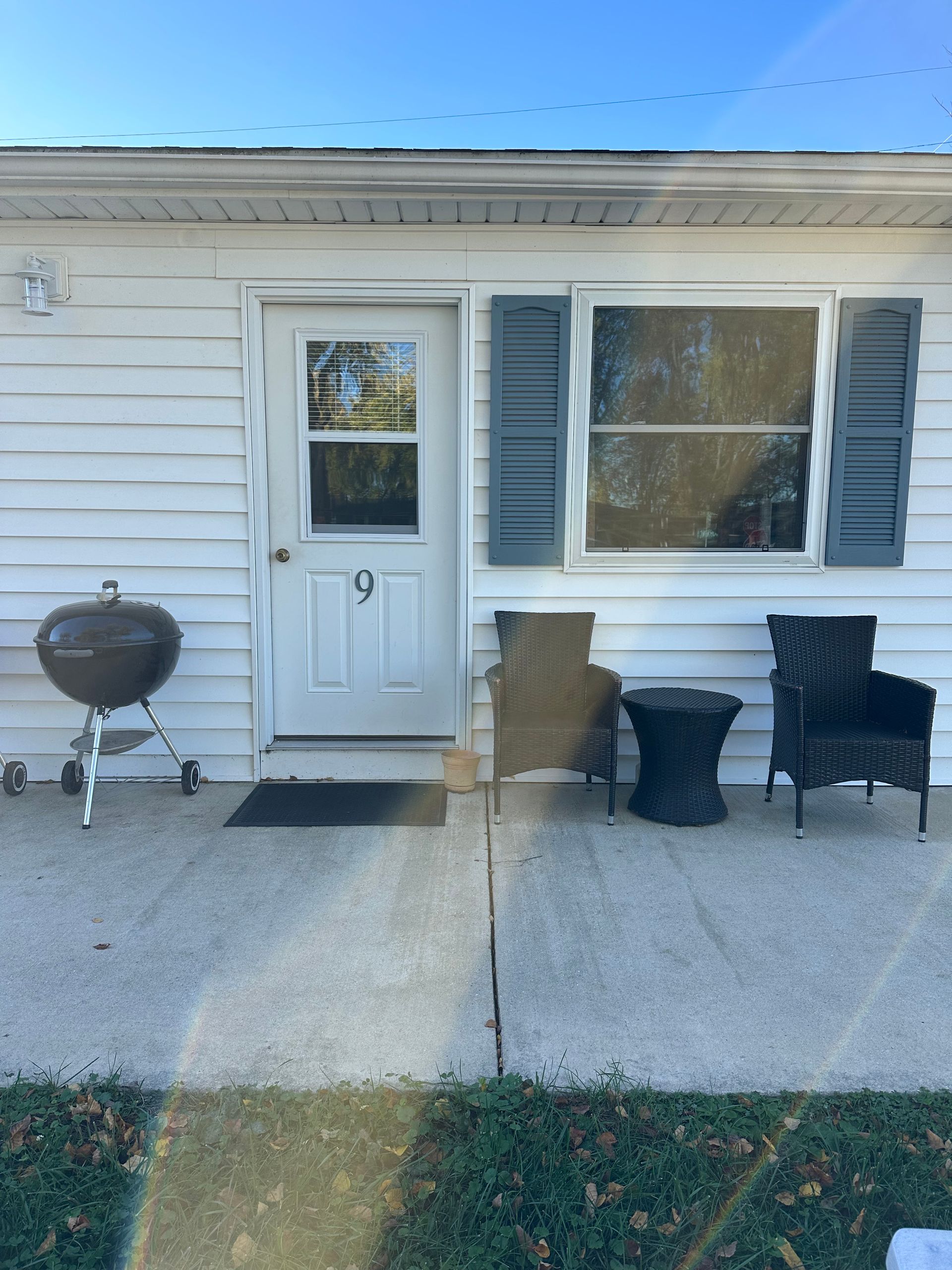 Exterior of a small white building with a door, window with gray shutters, and outdoor seating.