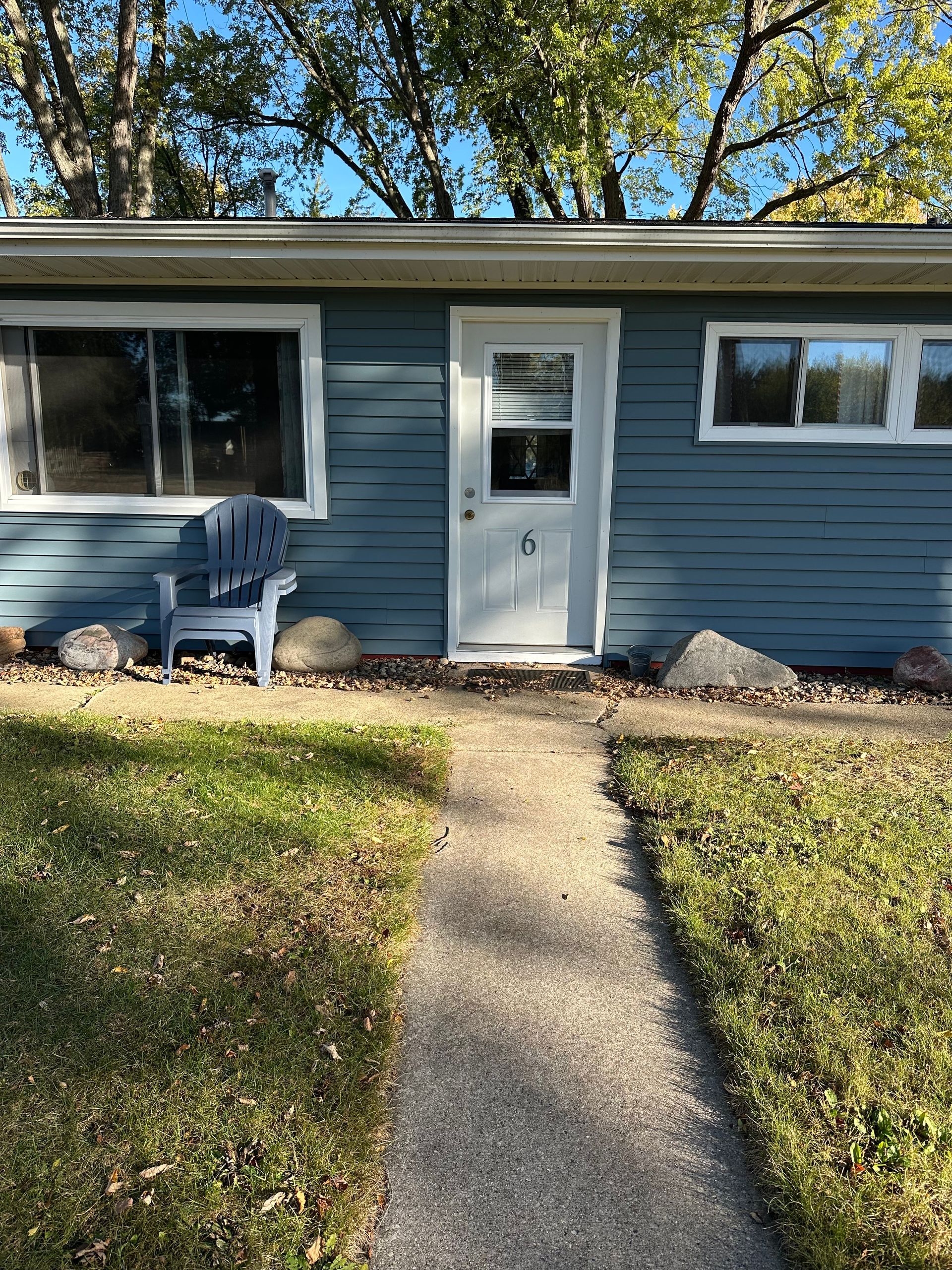 Blue house with a white door, windows, and an Adirondack chair on the grass.