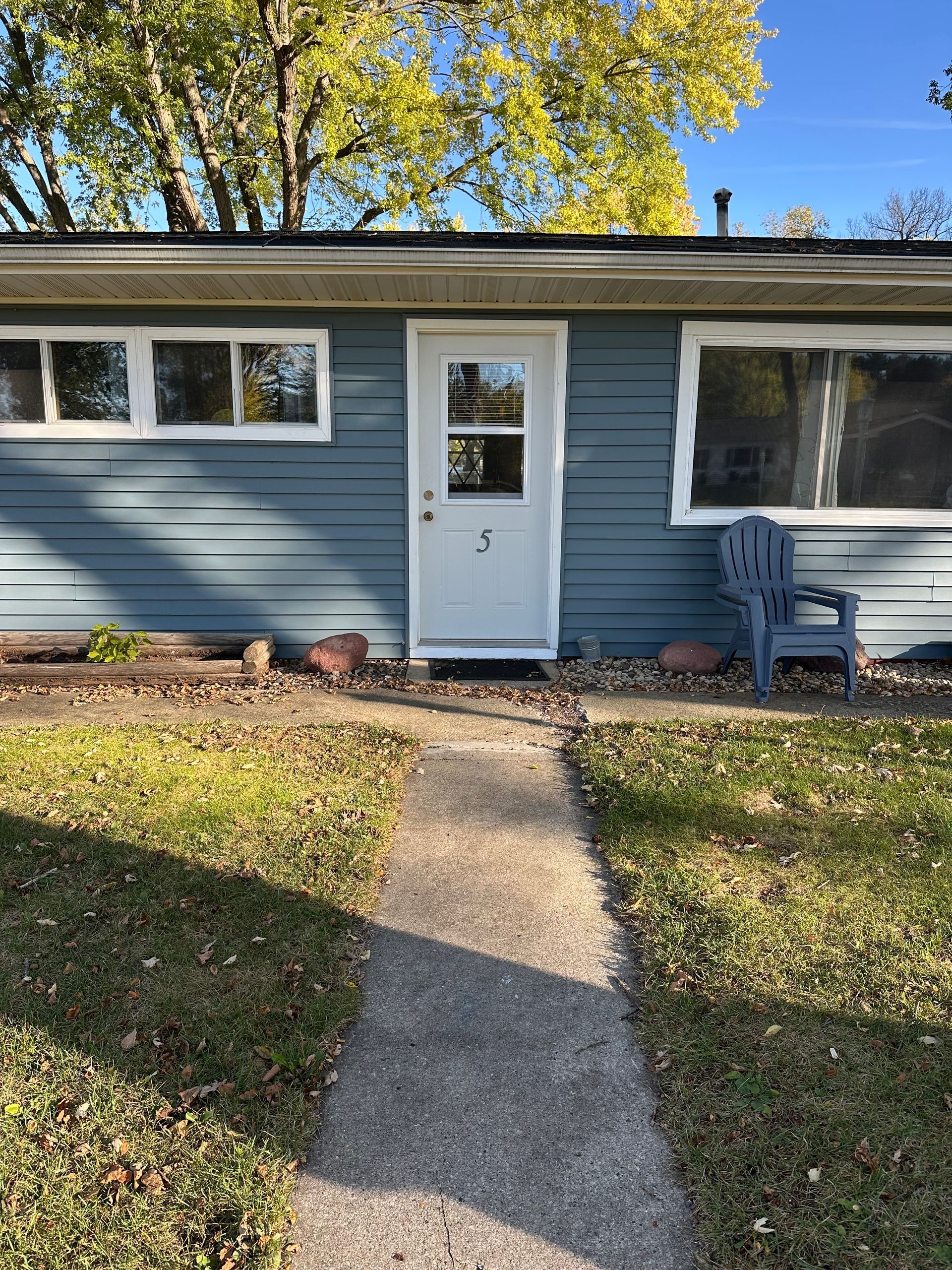 Blue house with a white door, windows, and a blue chair. A concrete path leads to the entrance.