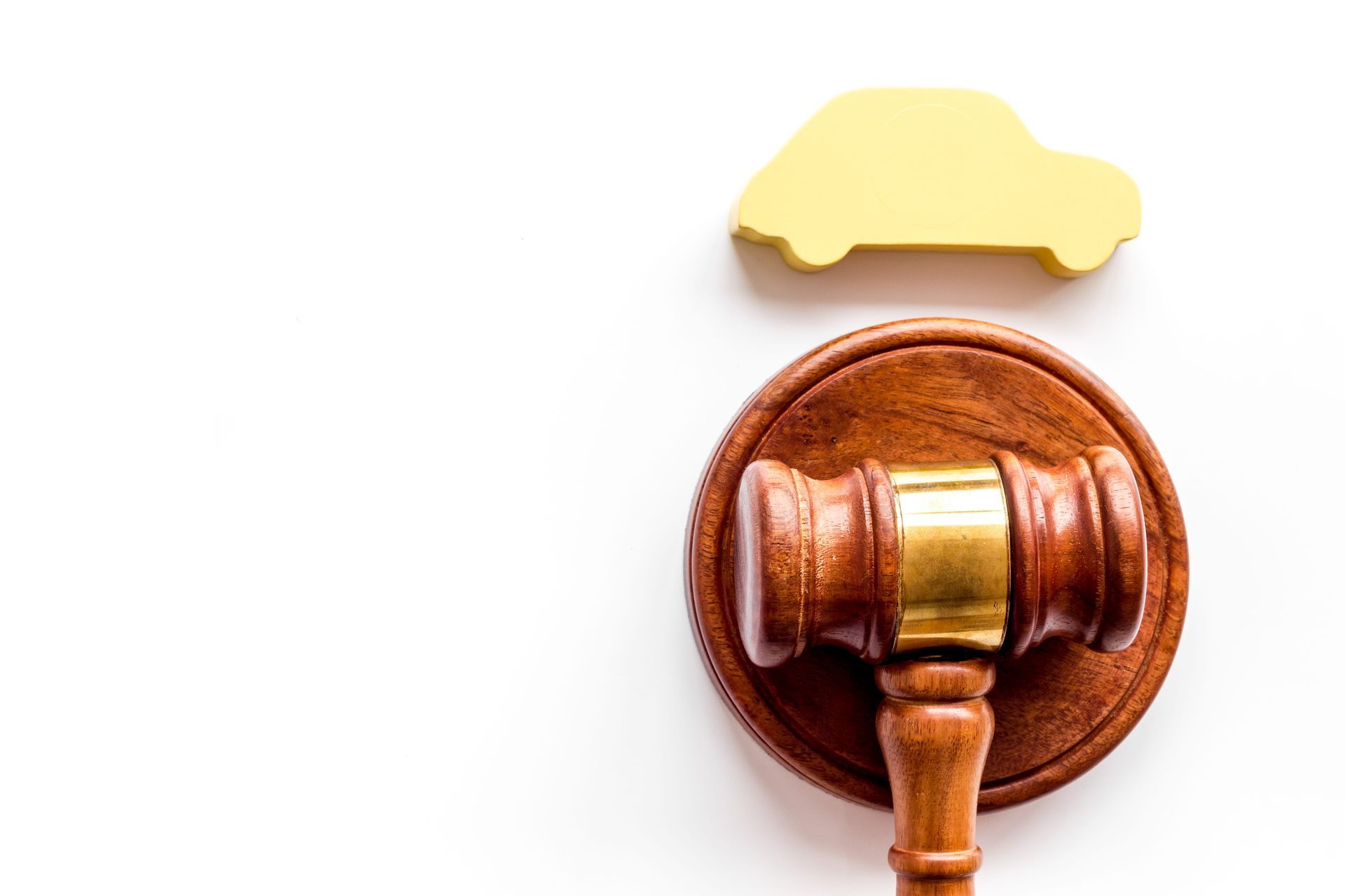 A wooden judge's gavel resting on its sounding block next to a small, yellow car silhouette on a white background.
