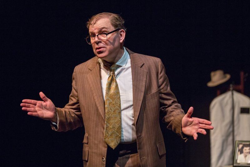 Bernie wearing a brown suit, gold tie and white shirt  while telling a story.