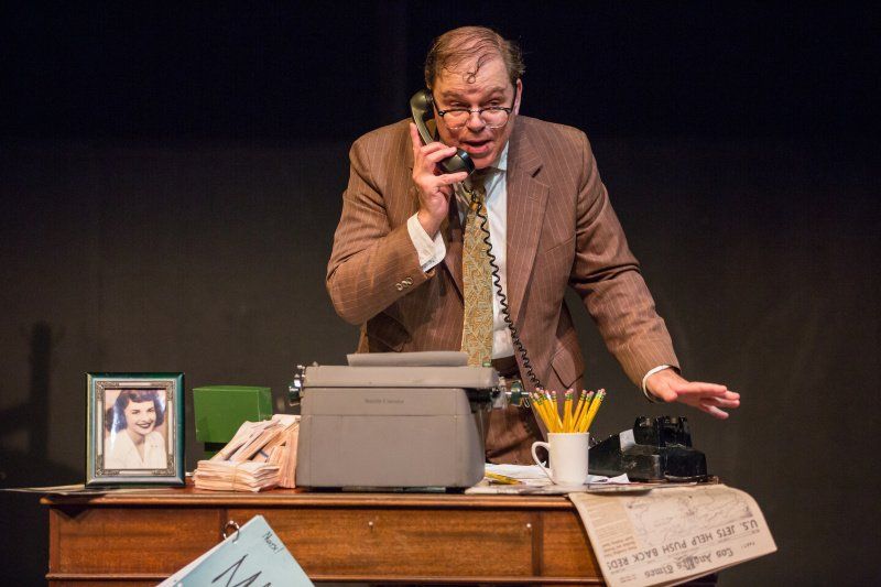 Bernie standing behind his desk excitedly talking on phone.