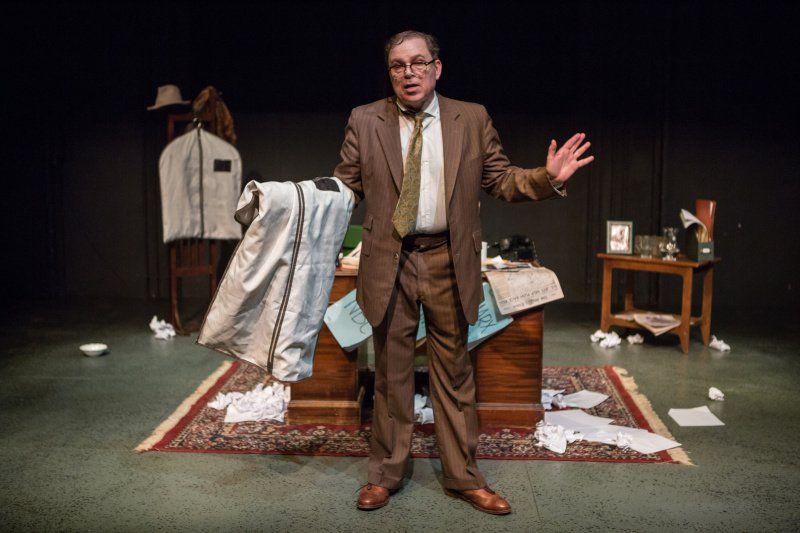 Bernie  in his messy office holding garment bag and telling a story.