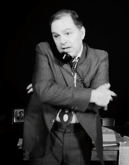 Bernie standing in front of desk with arms crossed and phone to ear