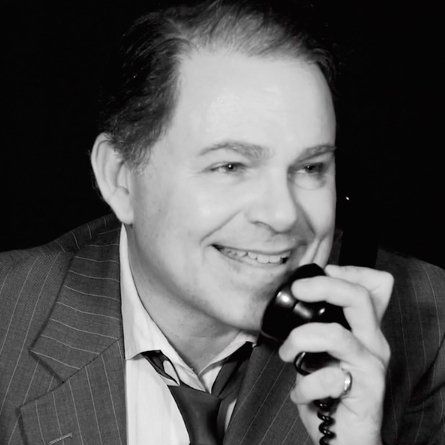 Bernie smiling in close-up while holding phone to left ear.