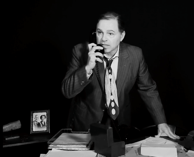 Bernie standing behind desk holding phone in right hand while on a call.