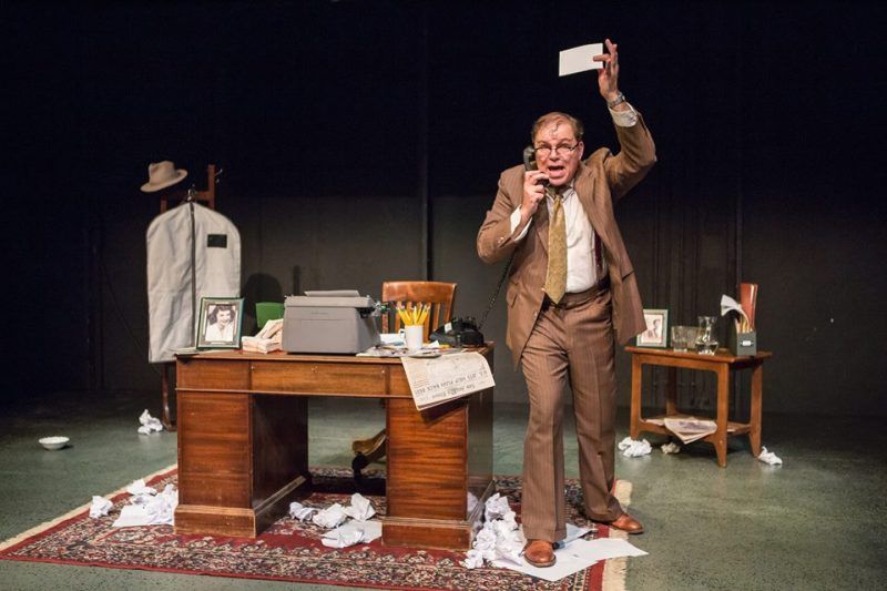 Bernie next to his desk holding phone with right hand and index card with left.