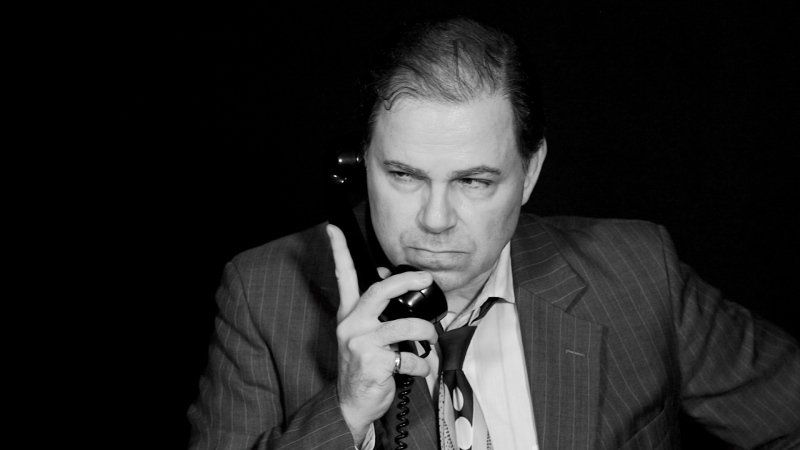 Bernie Lutz  looking  upset as he hears news on the phone he's holding in right hand.