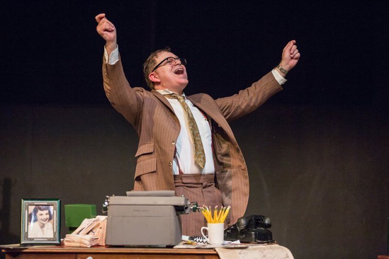 Bernie standing behind his desk raising both arms  and smiling