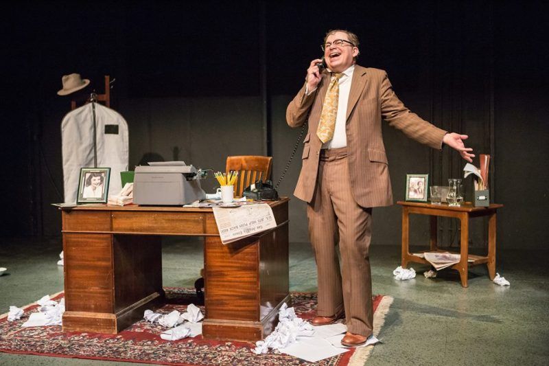 Bernie standing next to his desk talking on the phone and smiling and laughing.