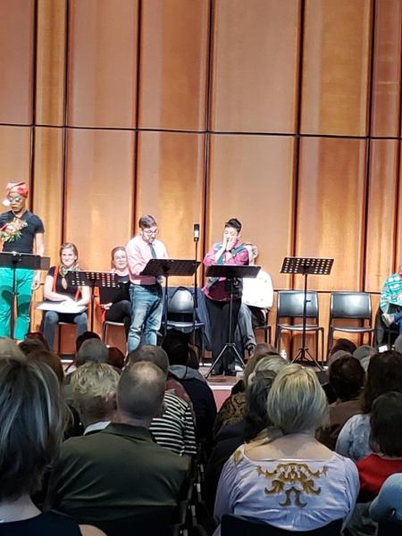 3 actors at standing at music stands on stage while 3 seated actors watch