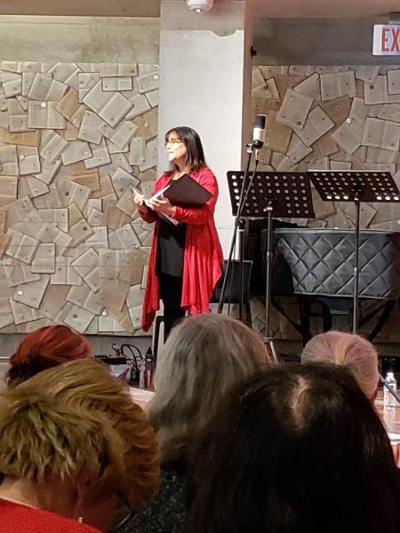 Woman in red sweater and black outfit holding a script to narrate scene