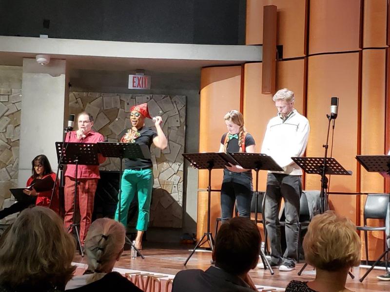 Seated woman in red sweater  and 4 actors standing at music stands