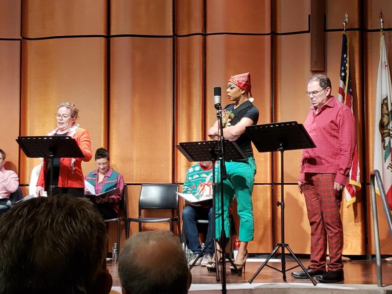 Woman in red jacket talking to 2 actors during a scene
