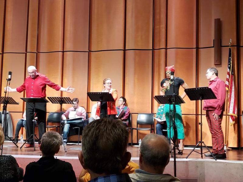Man in red shirt with arms open wide talking to 3 actors during a scene