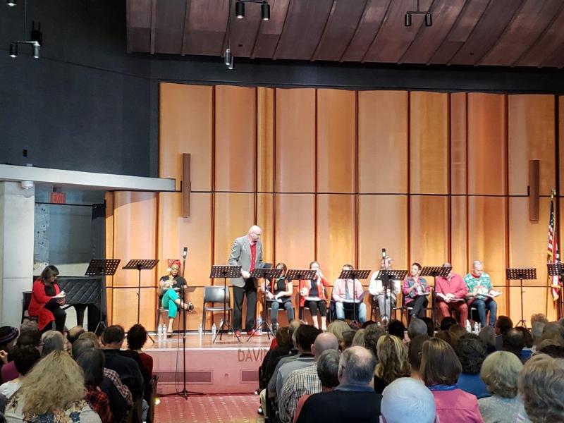 Ruff in grey jacket welcomes attendees to play reading at San Diego Main Library