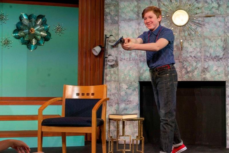Young man in blue shirt pointing a gun at his sister.