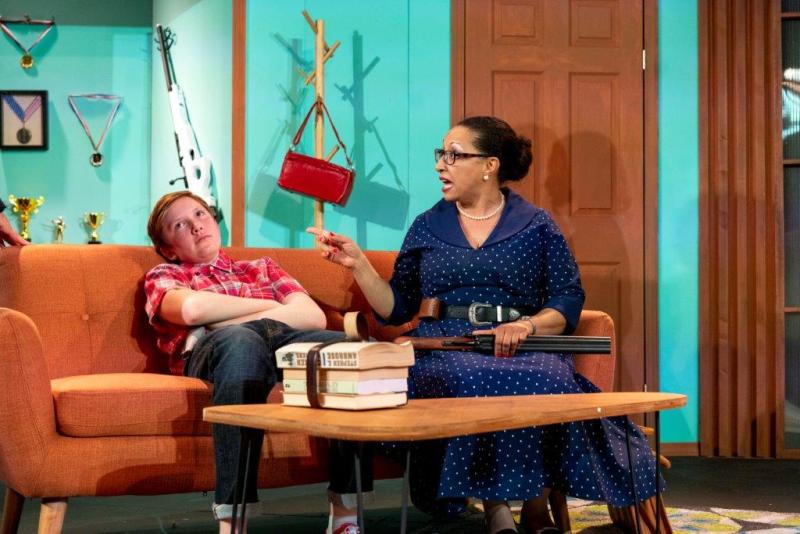 Social worker in blue polka-dot dress and young man in red-checked shirt sitting on orange sofa.