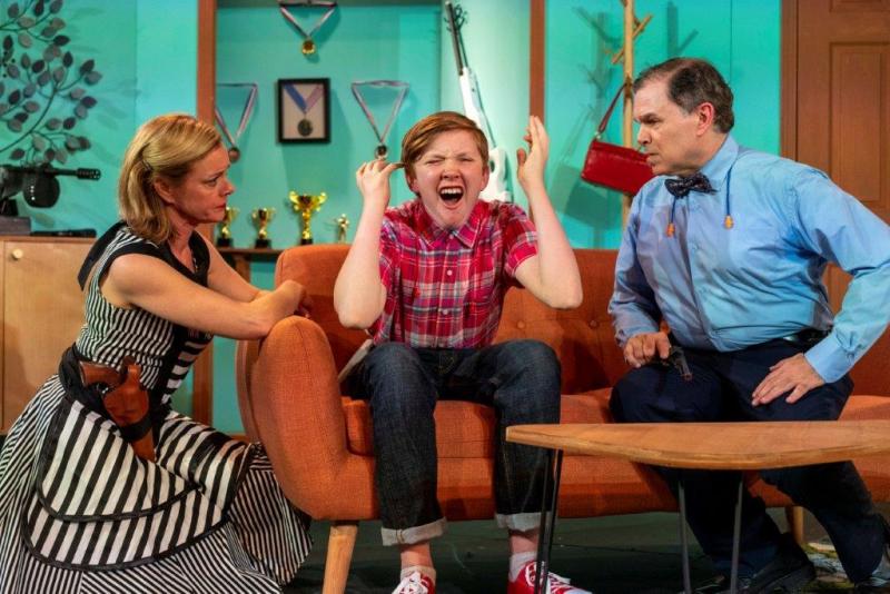 Mother and upset son wearing gun belts and father holding gun talking  on sofa.