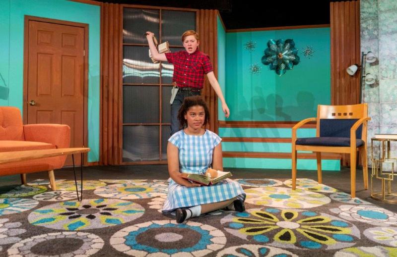 Young man standing in red-checked shirt ready to hit sister sitting on floor