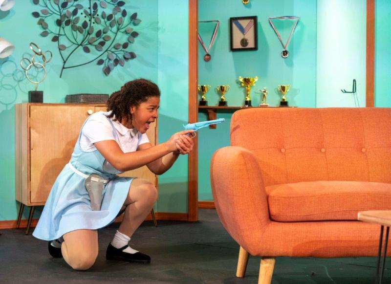 Young daughter in blue and white dress shooting a pretending to shoot a gun.