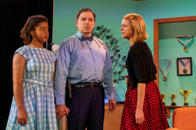 Young daughter in blue and white dress holding hands with father while mother speaks angrily