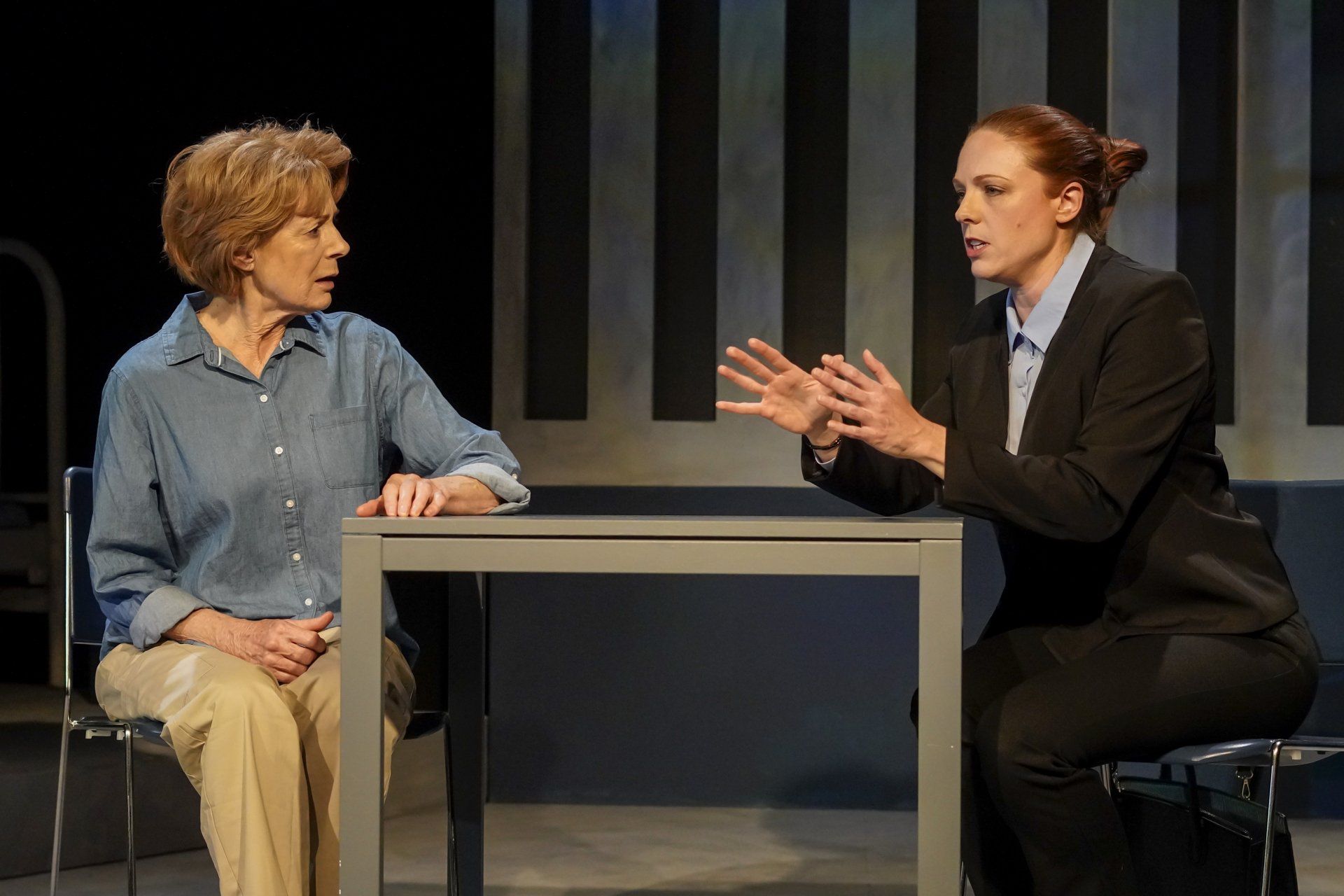 Two women are sitting at a table talking to each other on a stage .