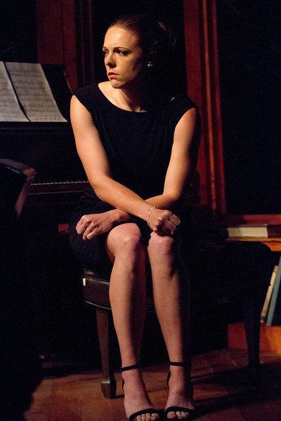 Woman in black dress sits on piano bench looking pensive
