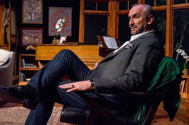 Man in grey suit jacket and blue jeans seated in a chair