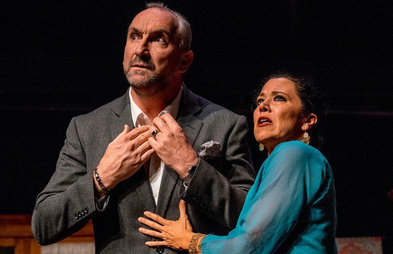 Man in grey suit jacket and white shirt and woman in blue outfit looking concerned