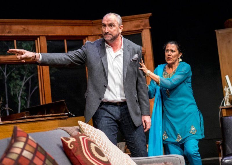 Angry man in grey suit jacket and white shirt being held back by woman in blue outfit