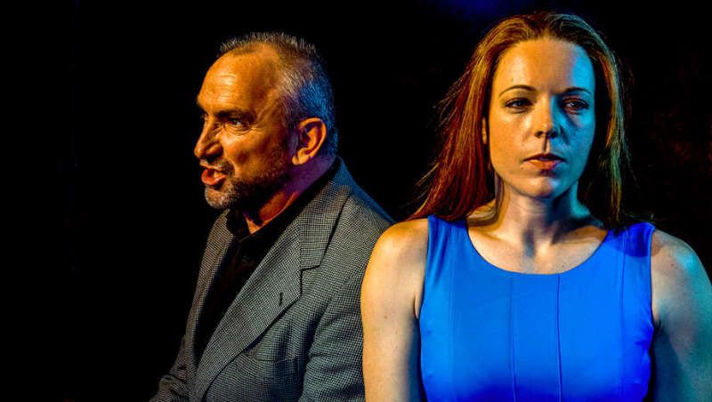 A man and a woman are standing next to each other in a dark room . The woman is wearing a blue dress.