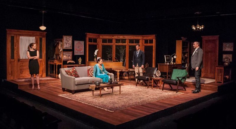Woman in black dress standing, woman in blue sitting and two men standing to side of sofa