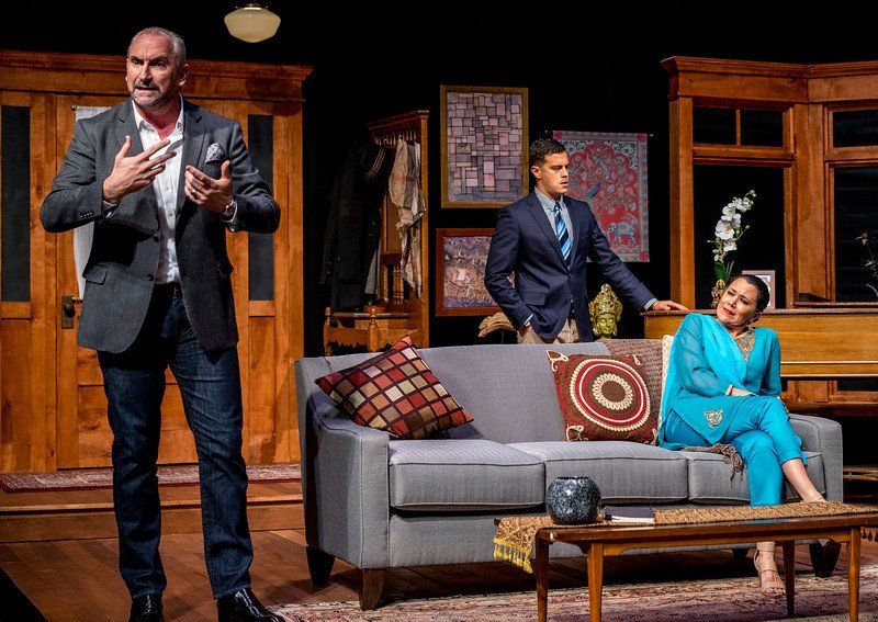 Man in grey suit gesturing while man in blue suit jacket and woman in blue listen