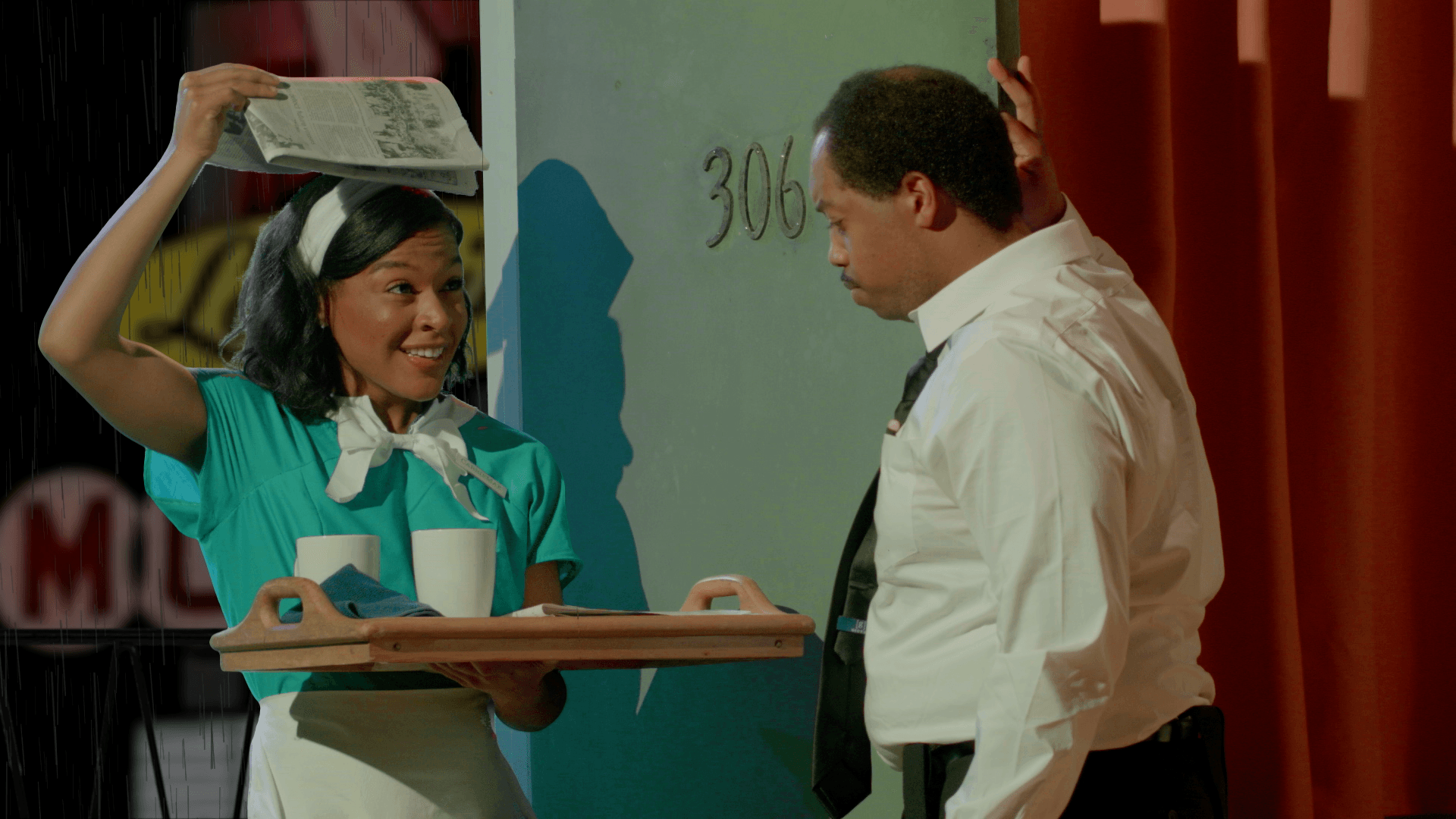 a man and a maid with a book on her head are standing next to each other on a stage .